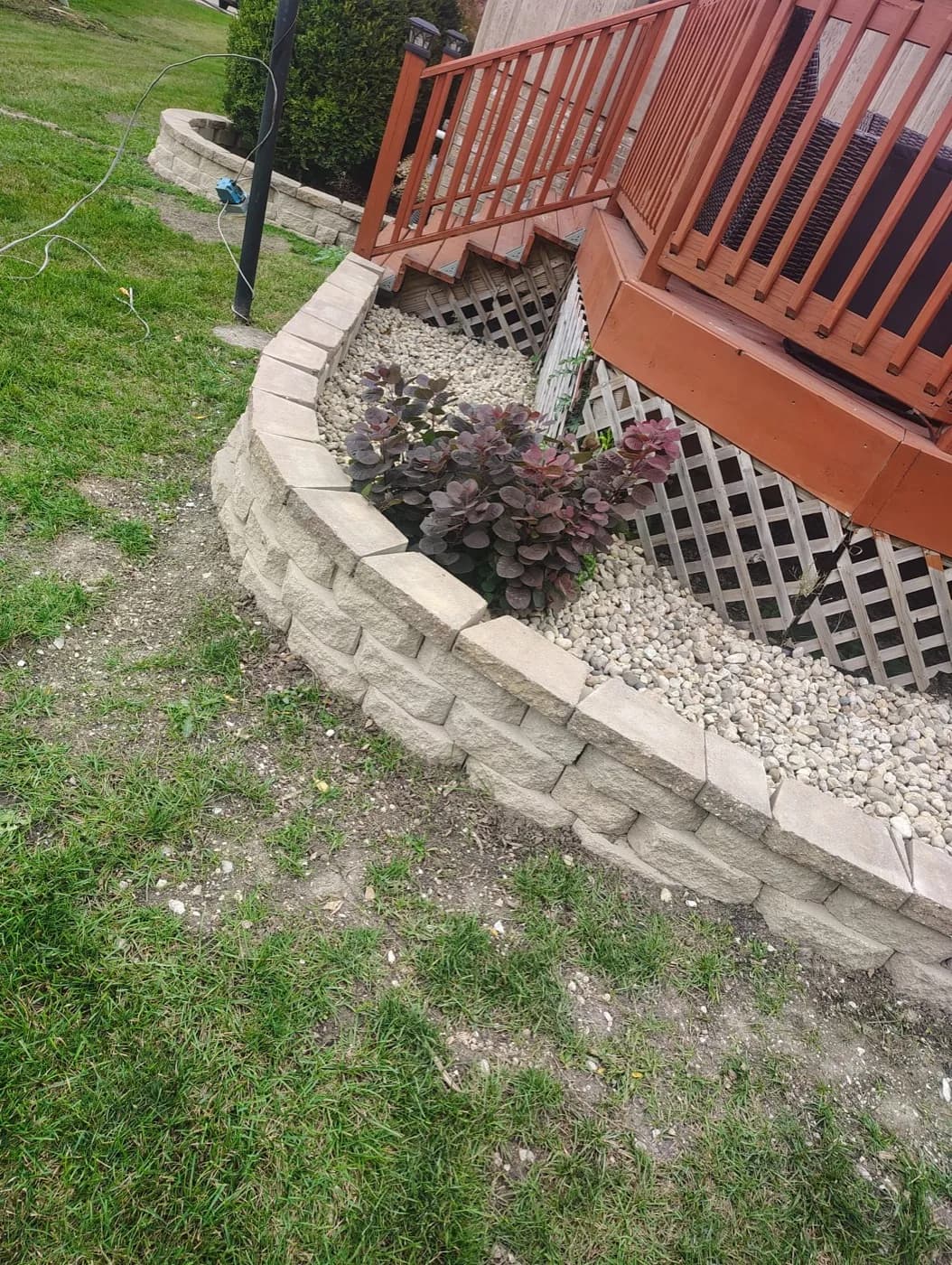 Curved block retaining wall filled with river rock beside a deck stair