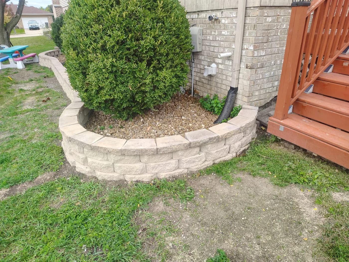 Block retaining wall wrapping an evergreen in decorative stone