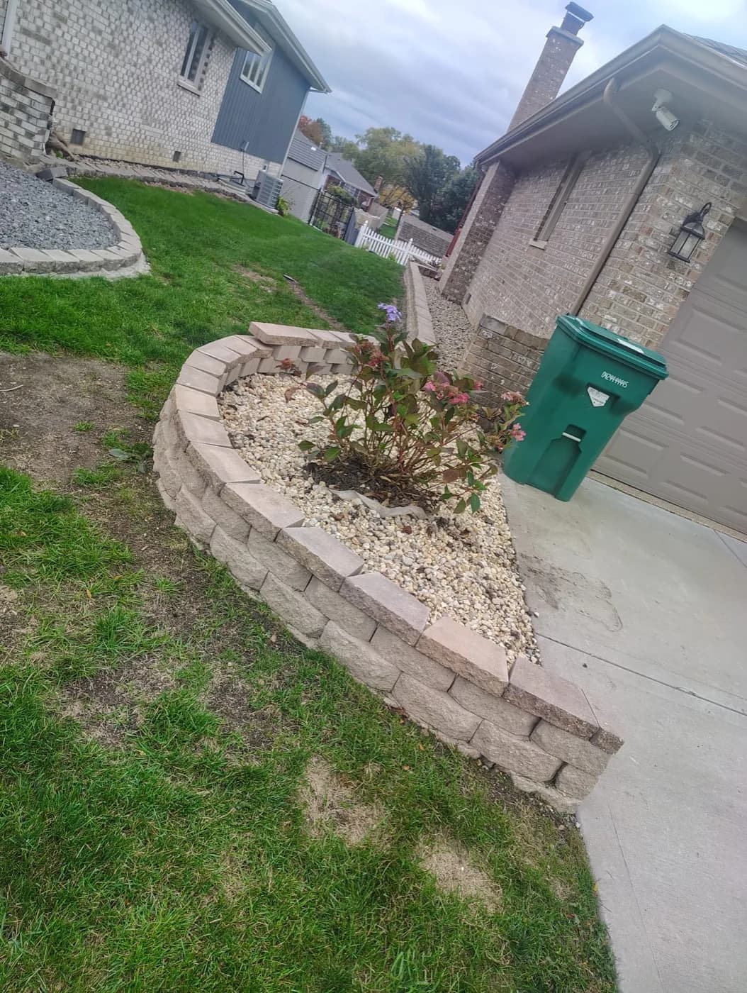 Tan block wall curving along a driveway with a shrub set in white stone