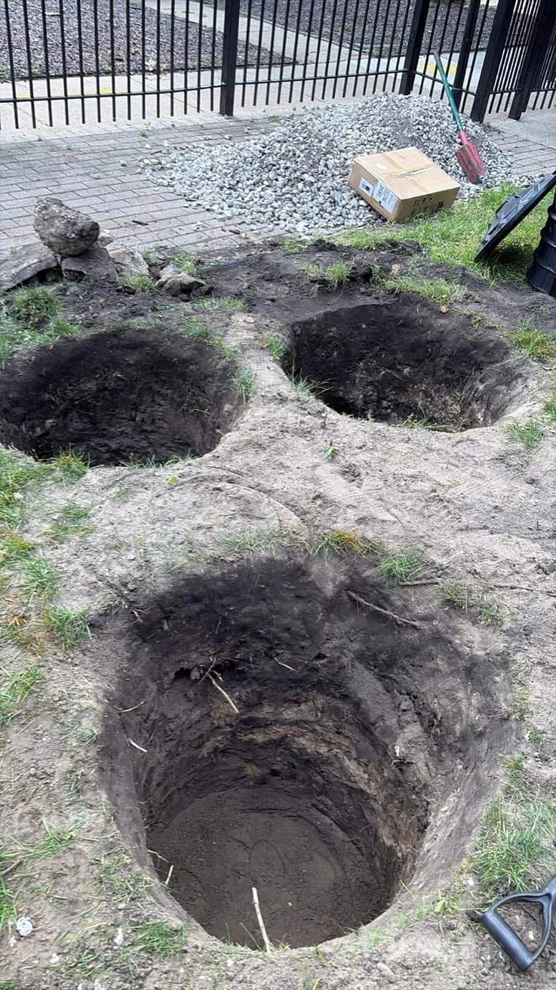 Drywell pits dug out in a yard with gravel staged nearby